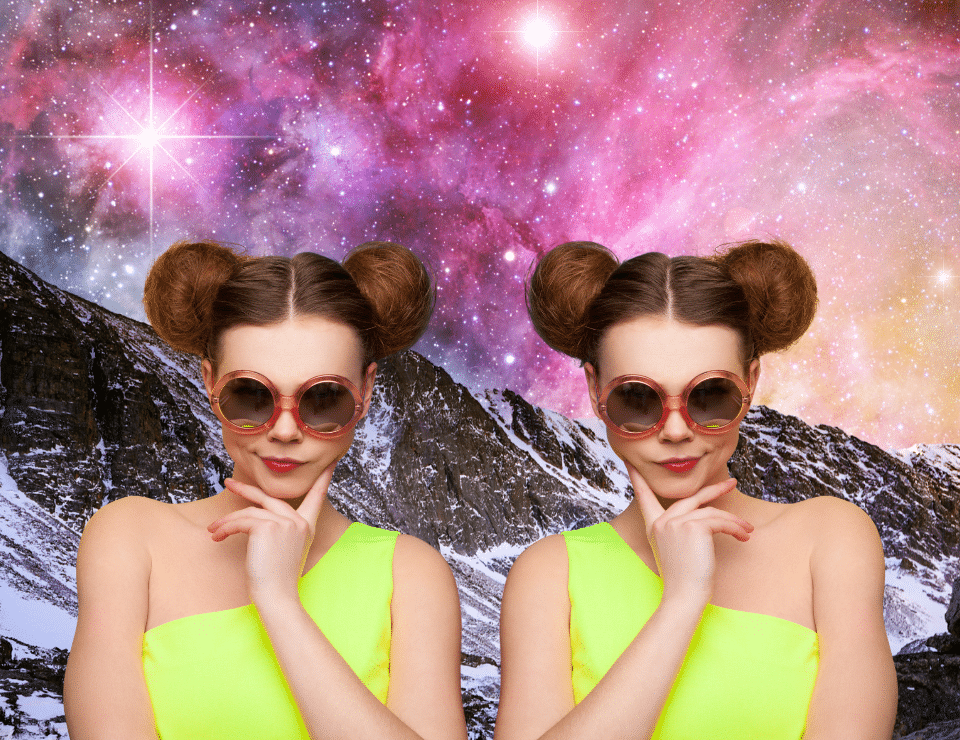 a pair of female twins with matching clothes, hair, and makeup standing in front of a mountain with space behind them