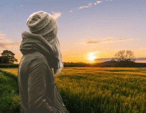 black and white image of a young woman looking away at a sun setting over a beautiful field