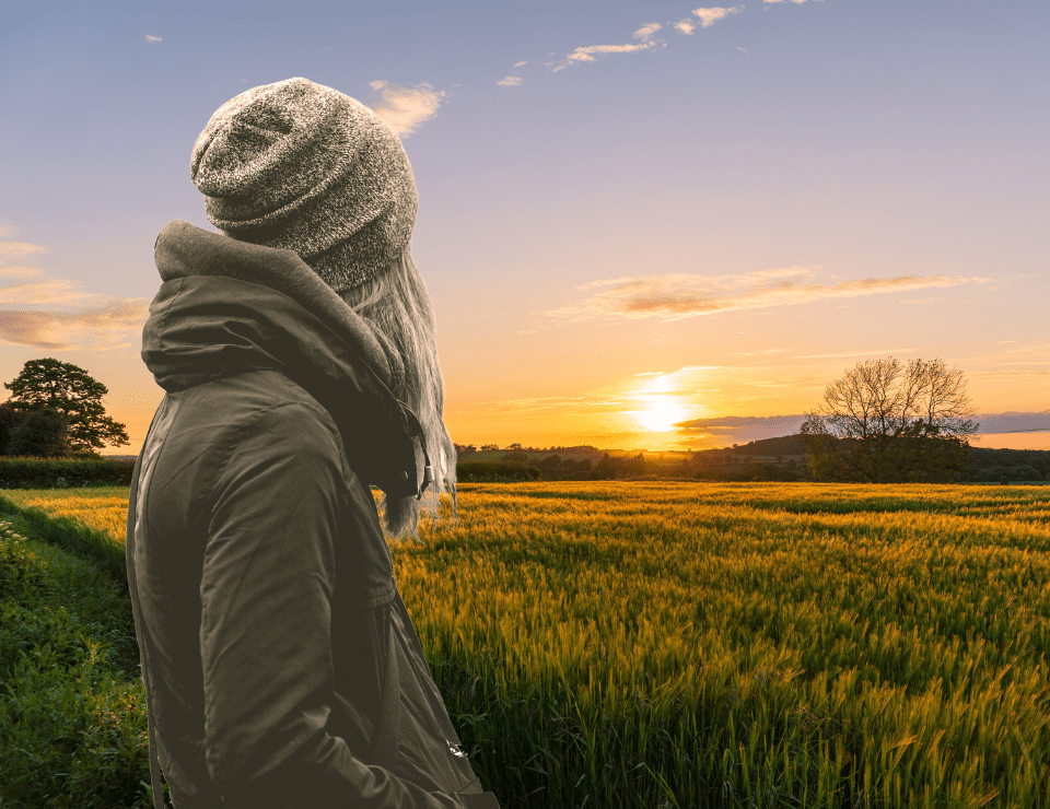 black and white image of a young woman looking away at a sun setting over a beautiful field